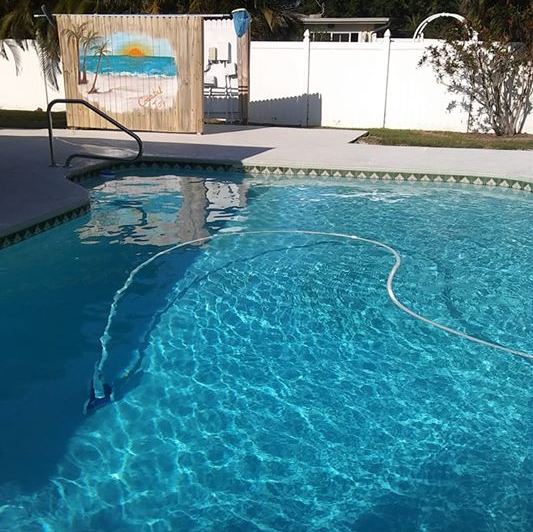 Backyard swimming pool with clear blue water, white fence, and a pool noodle floating inside