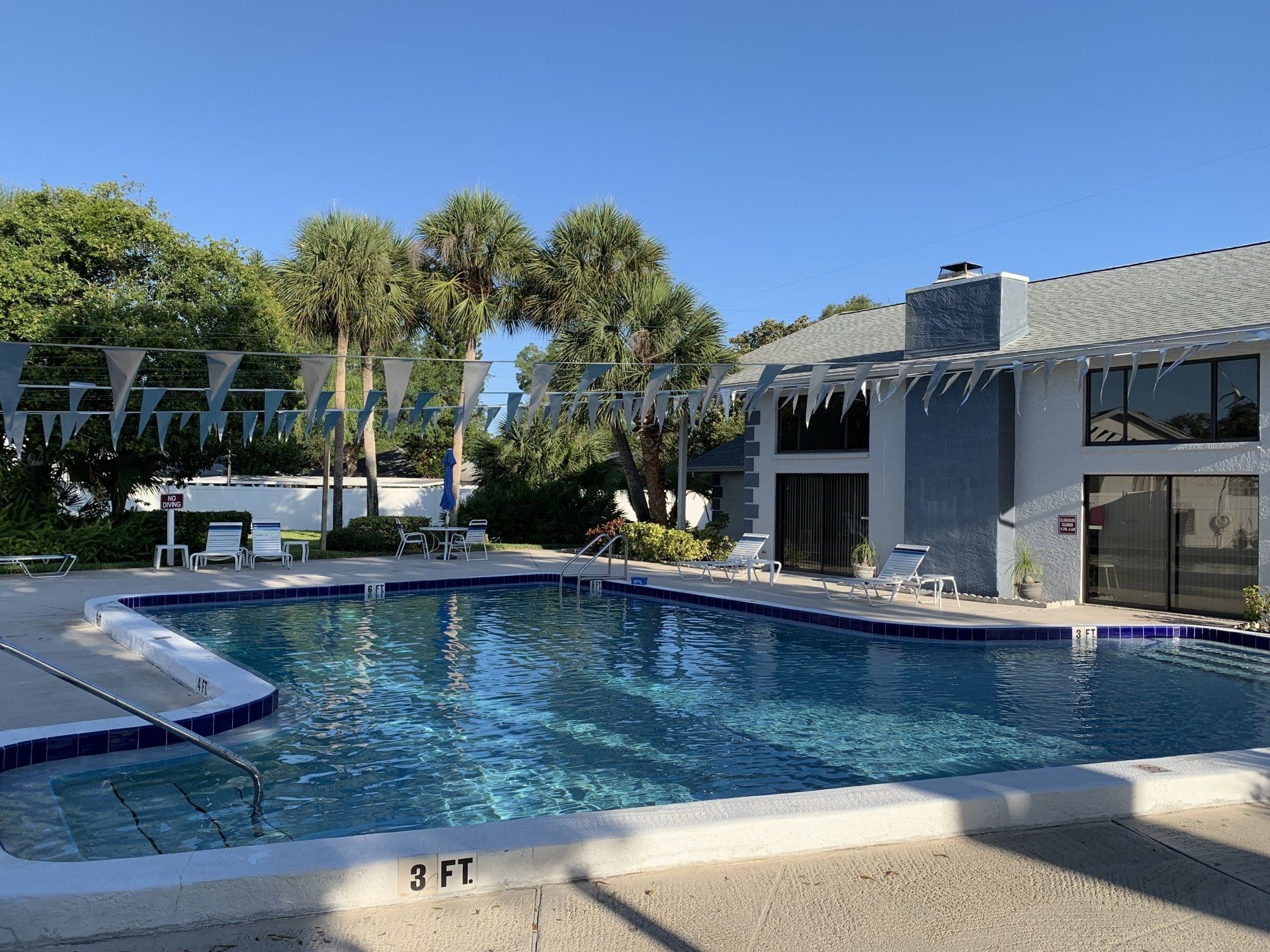 Outdoor swimming pool with blue water, lounge chairs, and palm trees beside a modern building.