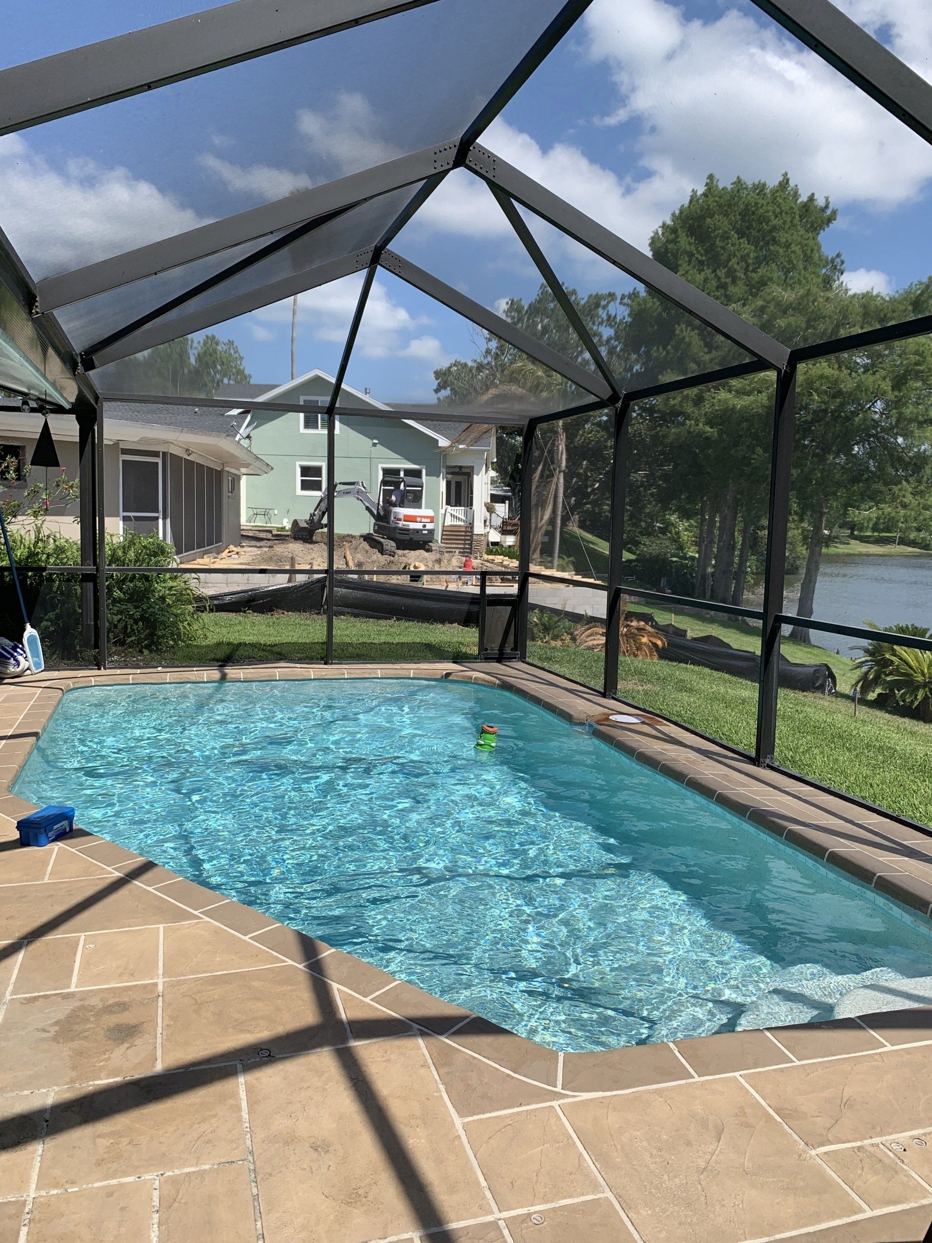 Screened-in backyard pool with blue water and tan patio under a sunny sky