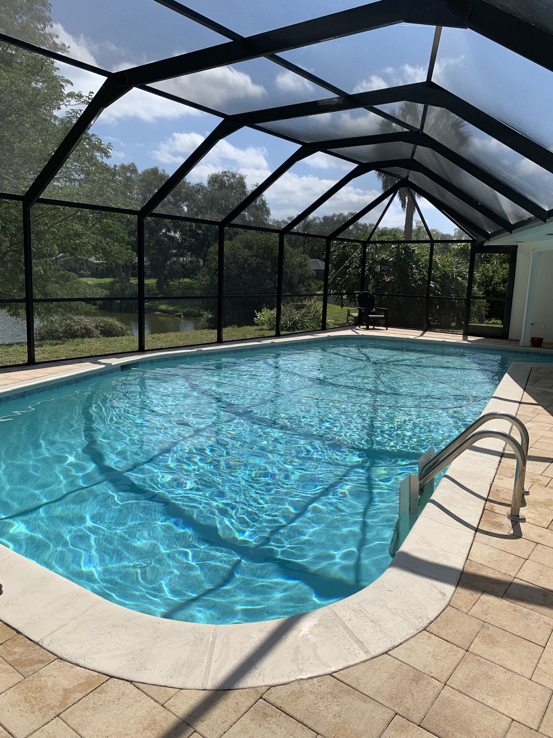 Screened-in backyard pool with blue water, tan pavers, and a black mesh enclosure under a sunny sky