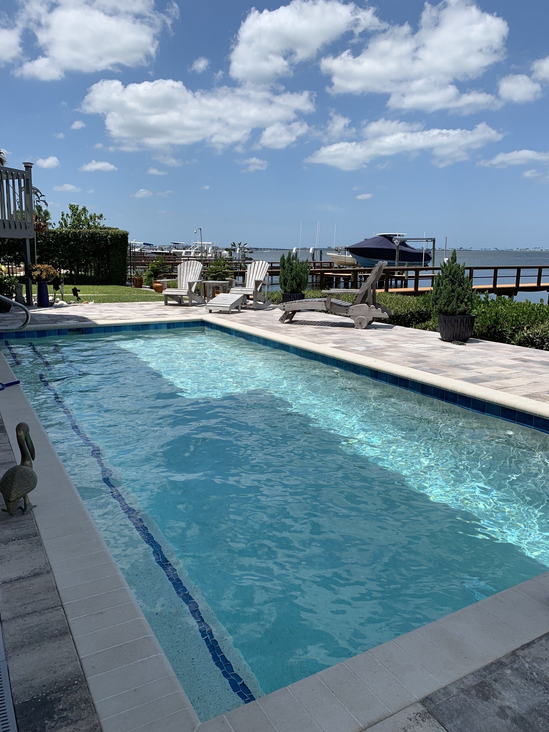 Rooftop pool with blue water beside lounge chairs under a partly cloudy sky.