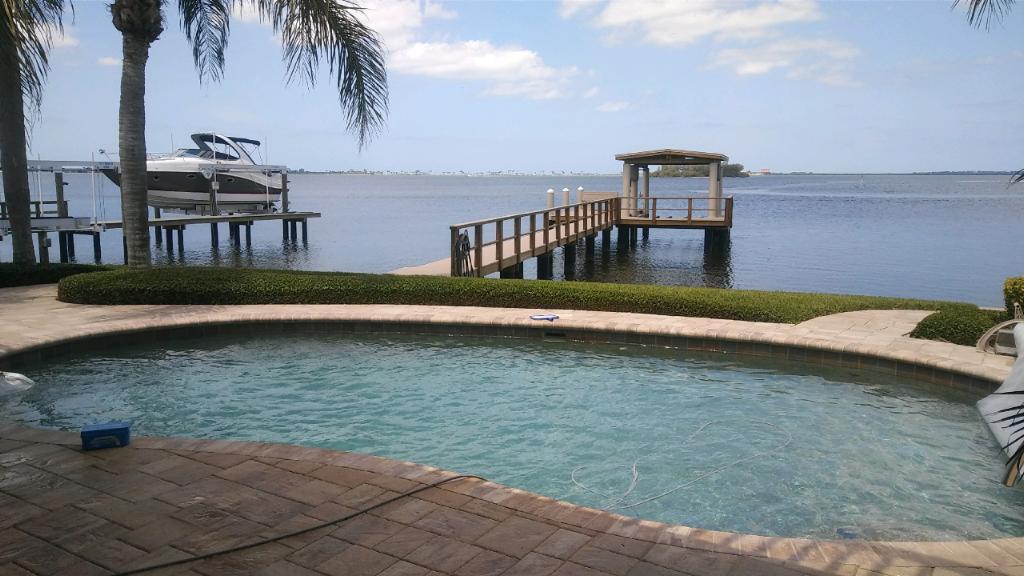 Backyard pool overlooking a calm bay with a wooden dock and small gazebo at sunset