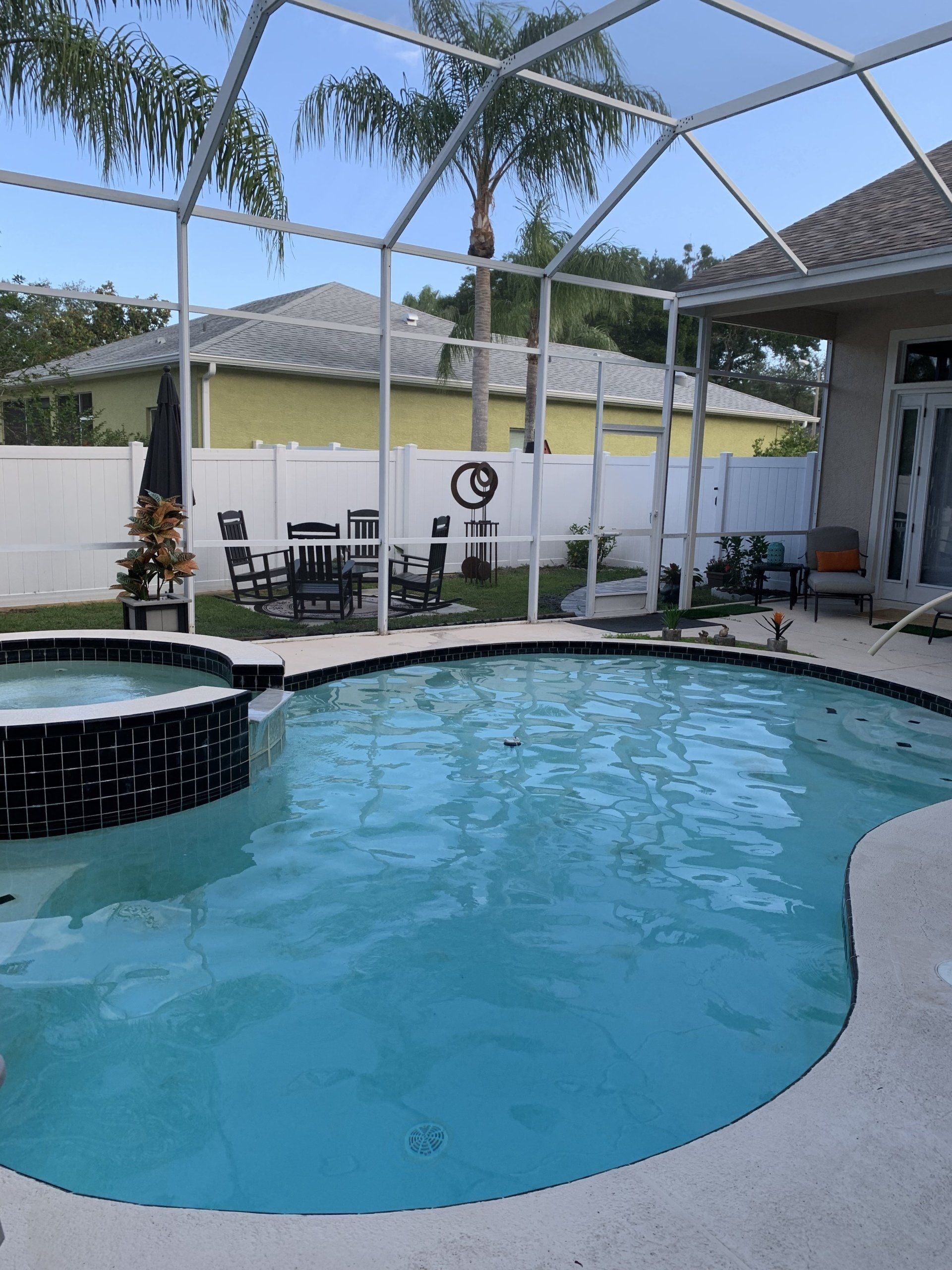 Backyard pool with white fence, screened enclosure, and patio chairs under a partly cloudy sky