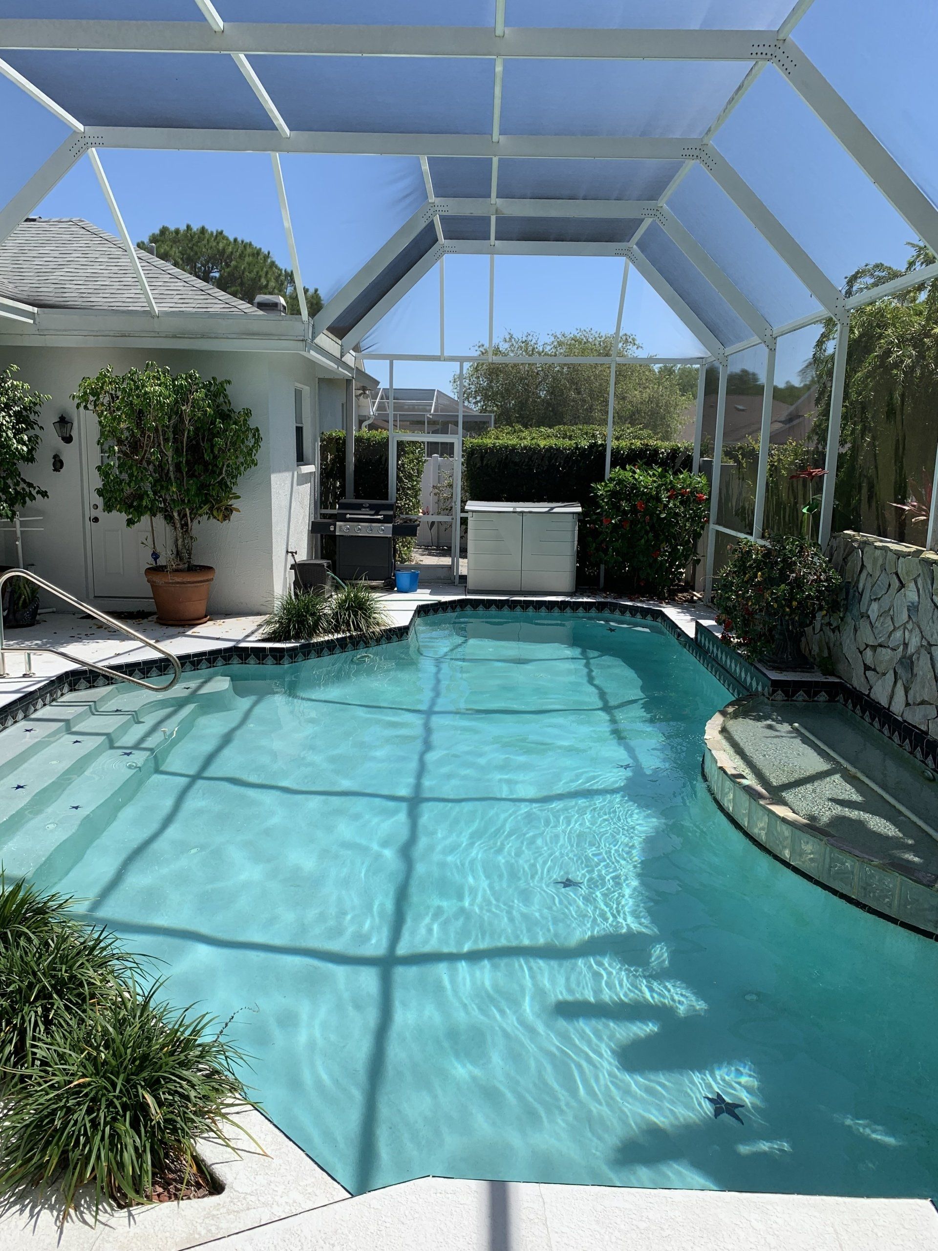 Screened backyard pool with turquoise water, patio seating, and white lanai structure