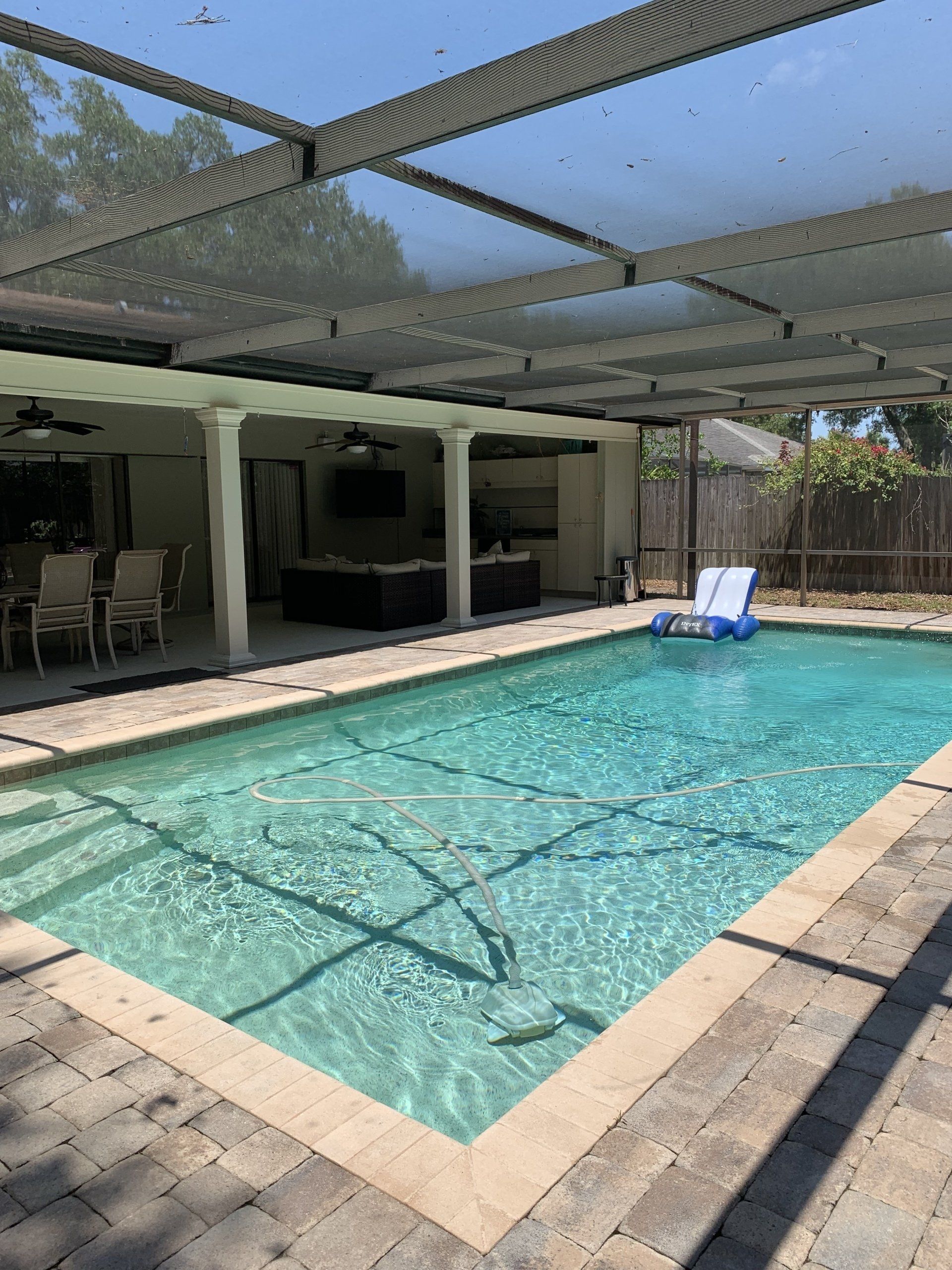 Backyard swimming pool with screened enclosure, patio, and a blue lounge chair in sunlight