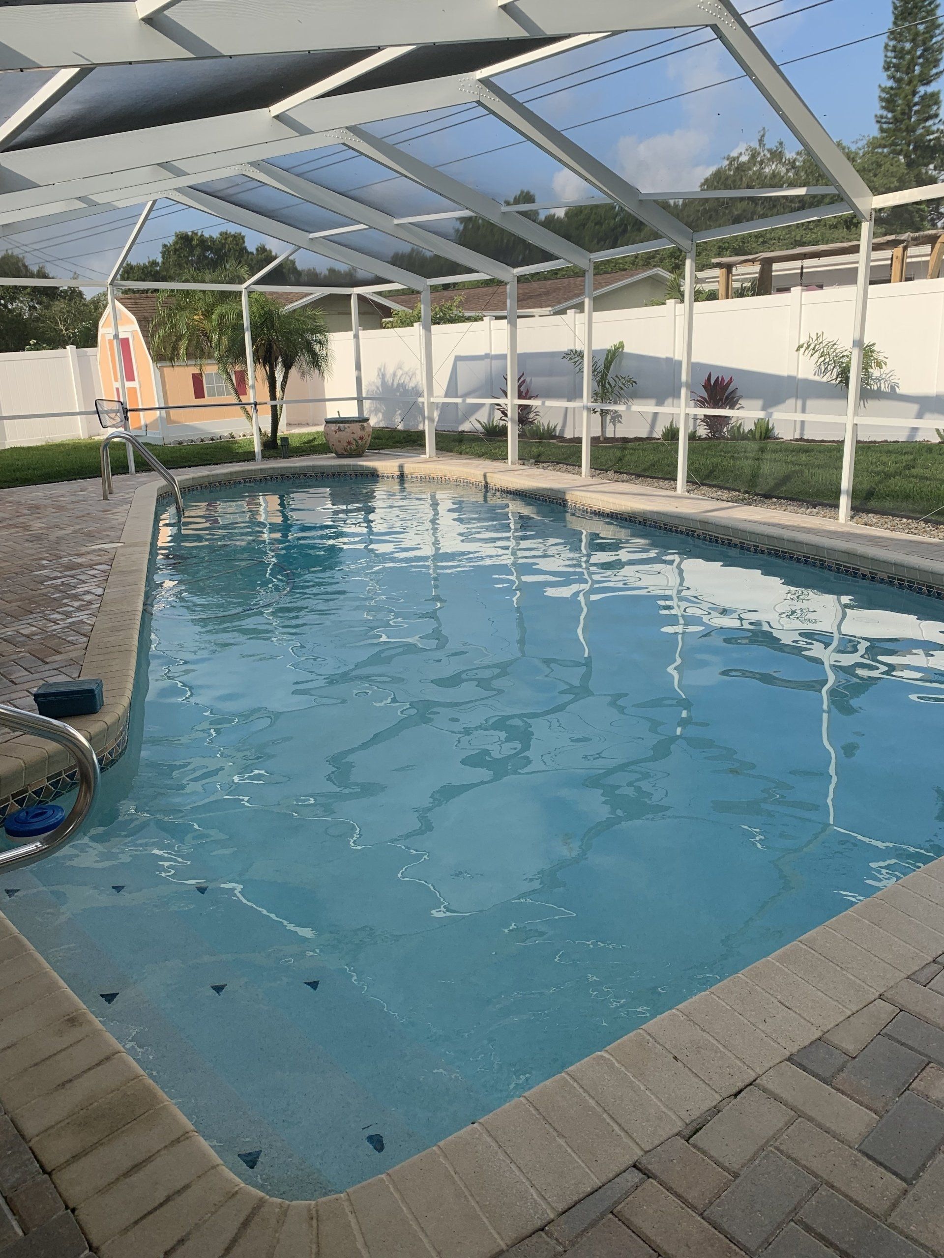 Backyard swimming pool under a white screened pergola, with paver deck and blue water.