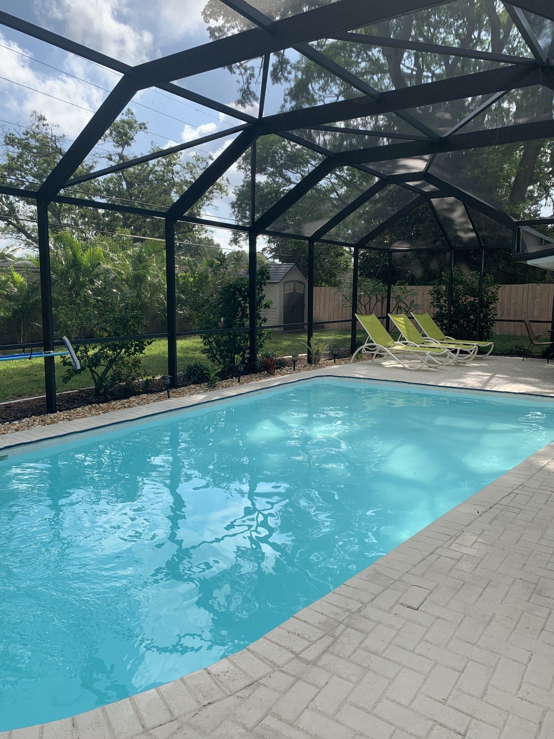 Screened outdoor pool with turquoise water beside lounge chairs and greenery
