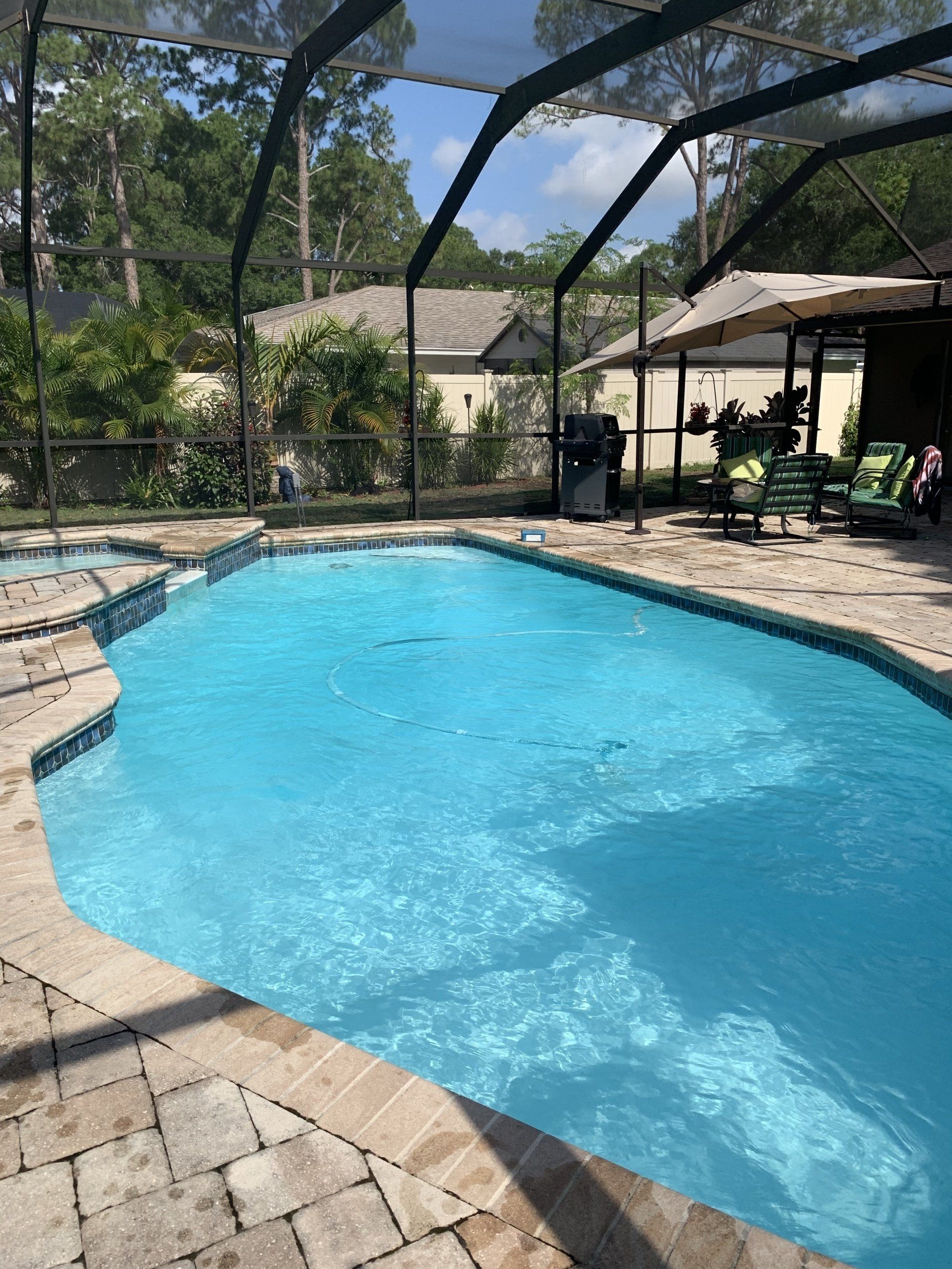 Backyard swimming pool with clear blue water, screened enclosure, and patio chairs under a shaded lanai