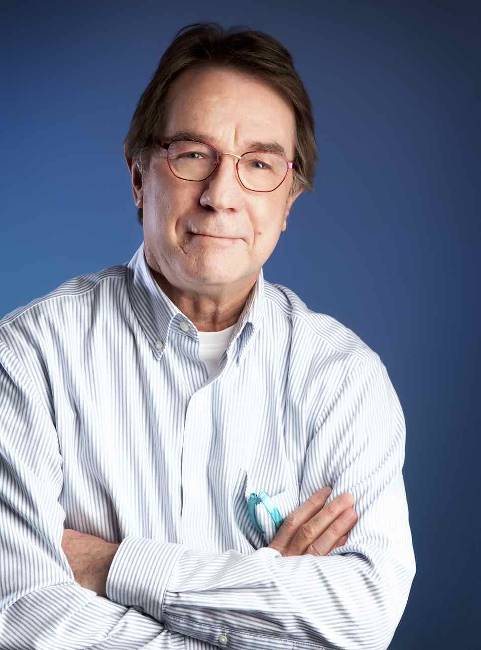 A man wearing glasses and a striped shirt is standing with his arms crossed.