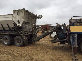 Une pompe à béton est attachée à un camion dans un champ de terre.