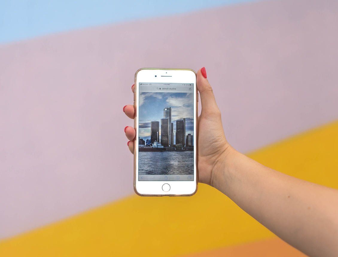 close up woman's hand holding a mobile phone in front of a striped colorful wall Hand holding a smartphone displaying a cityscape, against a colorful wall.