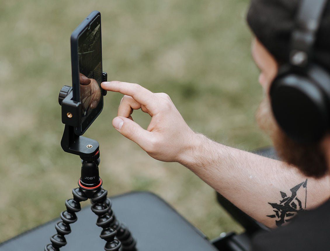 Image of a man using an iPhone on a tripod wearing headphones A man wearing headphones is holding a cell phone on a tripod.