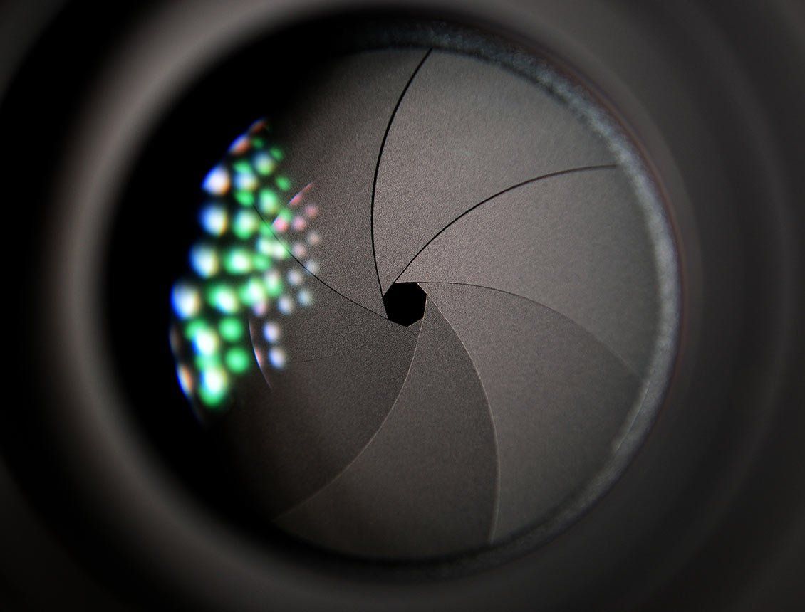 Image of a close up of a black camera aperture with colored light reflecting in lens A close up of the inside of a camera lens