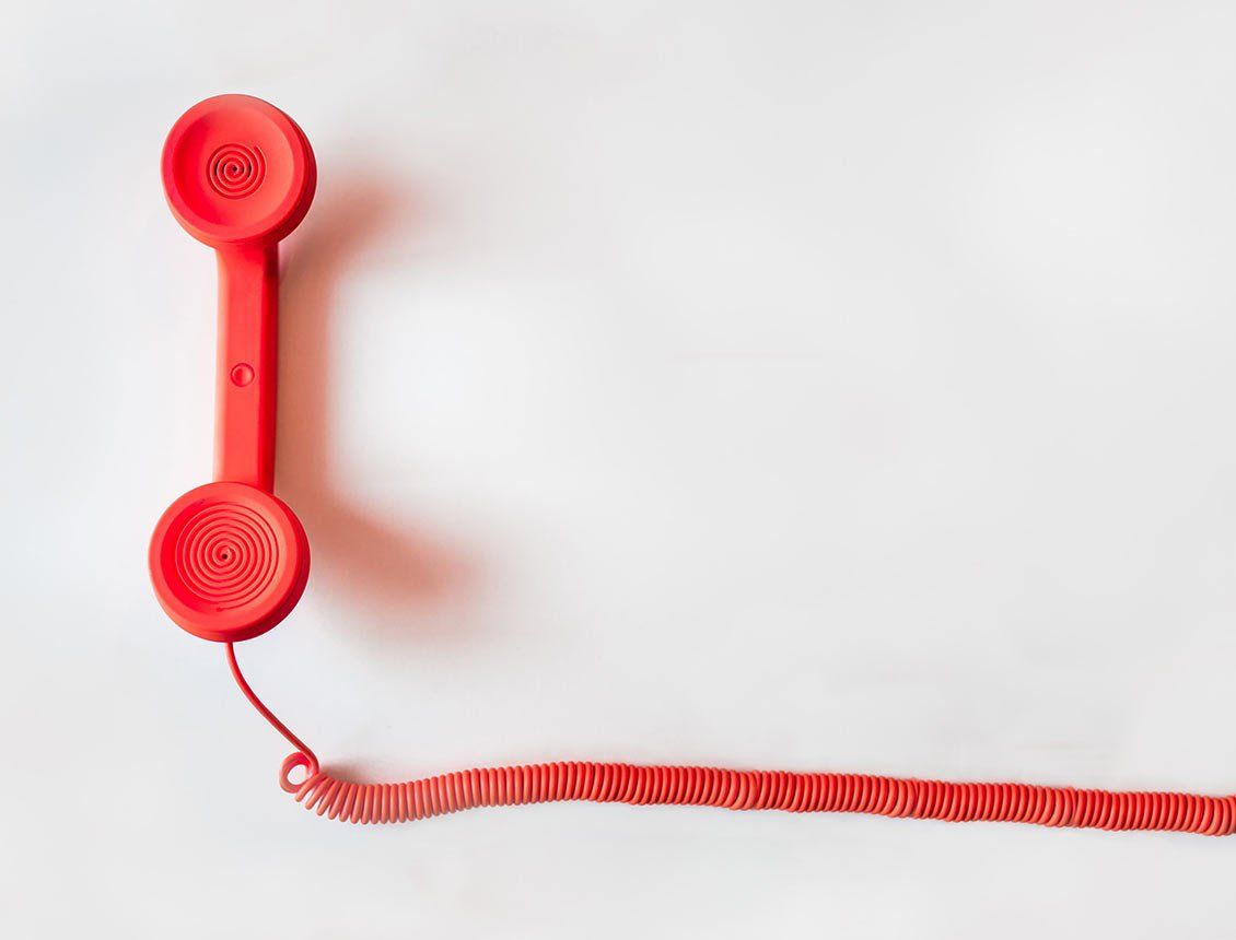 A red telephone with a red cord on a white background.