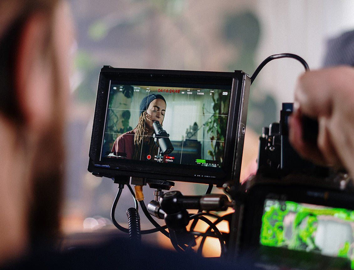 Close up of cinema video camera showing a signer on the camera monitor A man is recording a video of a woman singing into a microphone.