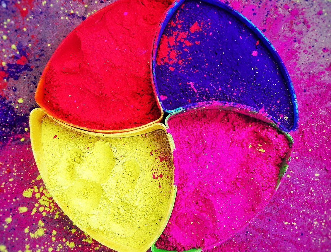 Brightly colored powders, red, yellow, blue, and pink, fill pie-shaped compartments, scattered on a purple surface.