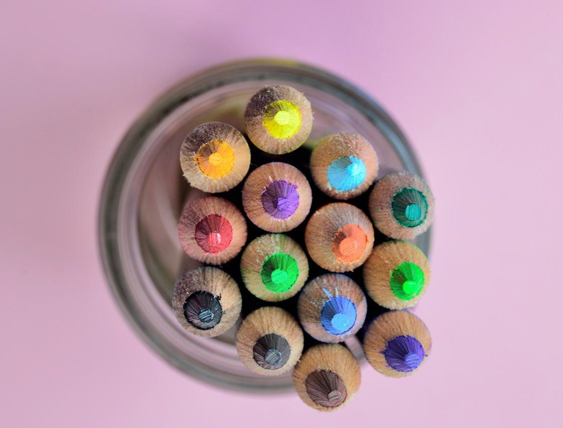 Top down close up image of colored pencils in jar A glass filled with colored pencils on a pink background