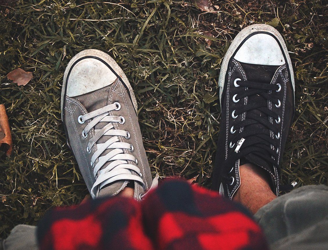 A person wearing a plaid hat and converse shoes is sitting on the grass.