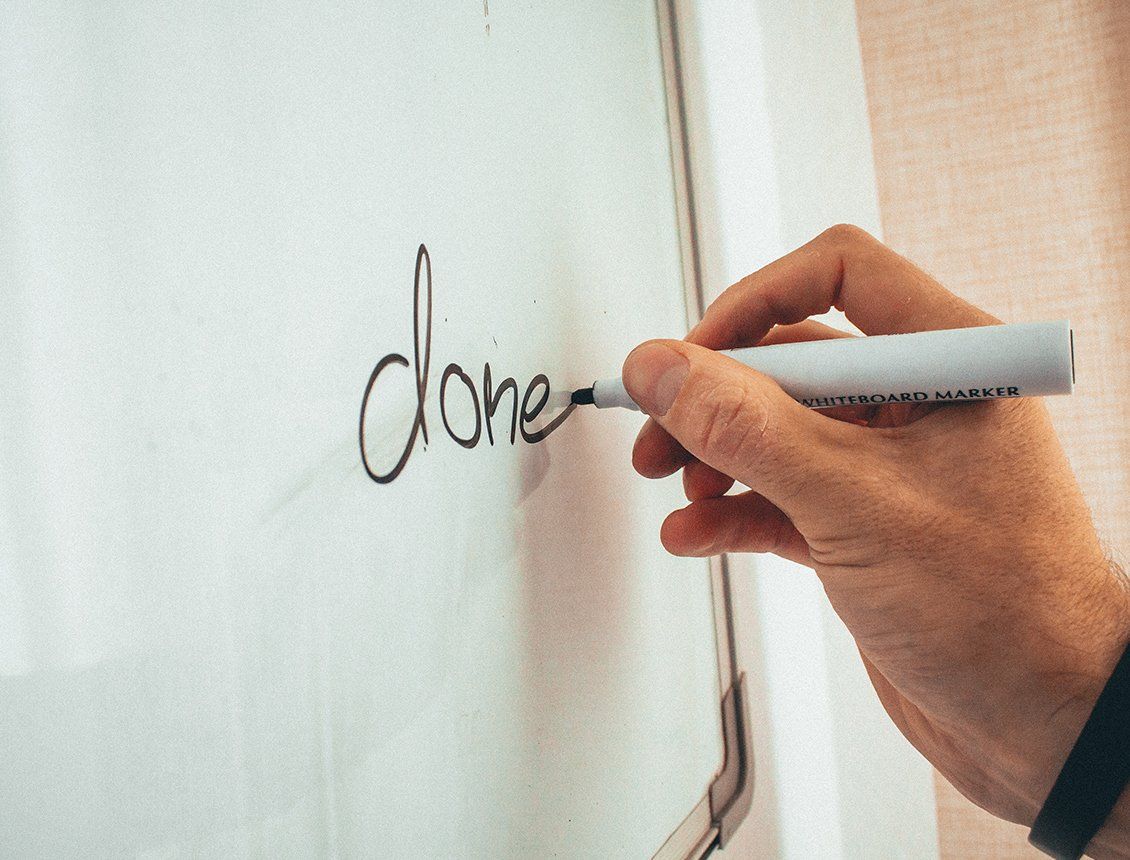 Close up whiteboard writing the word done A person is writing the word done on a white board with a marker.