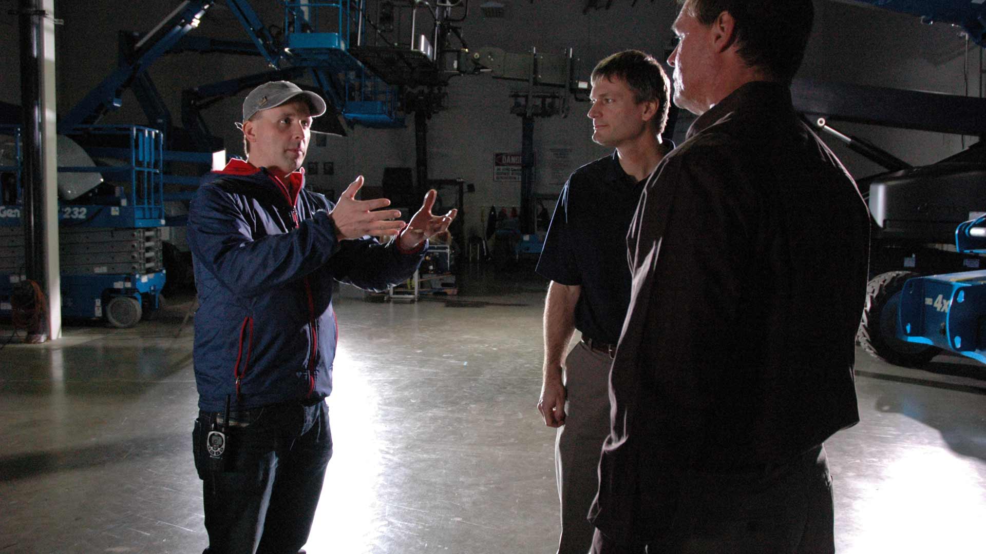 Genie Brand Film Behind the Scenes Matthew Billings Directing Three men are standing in a dark room talking to each other