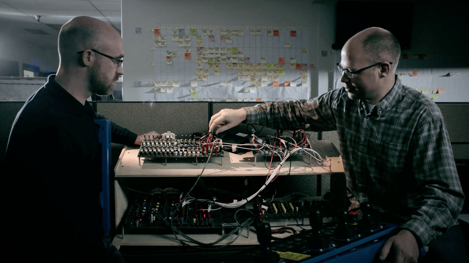 Genie Brand Film Engineers w/ Electronics Two men are working on a computer in an office cubicle.