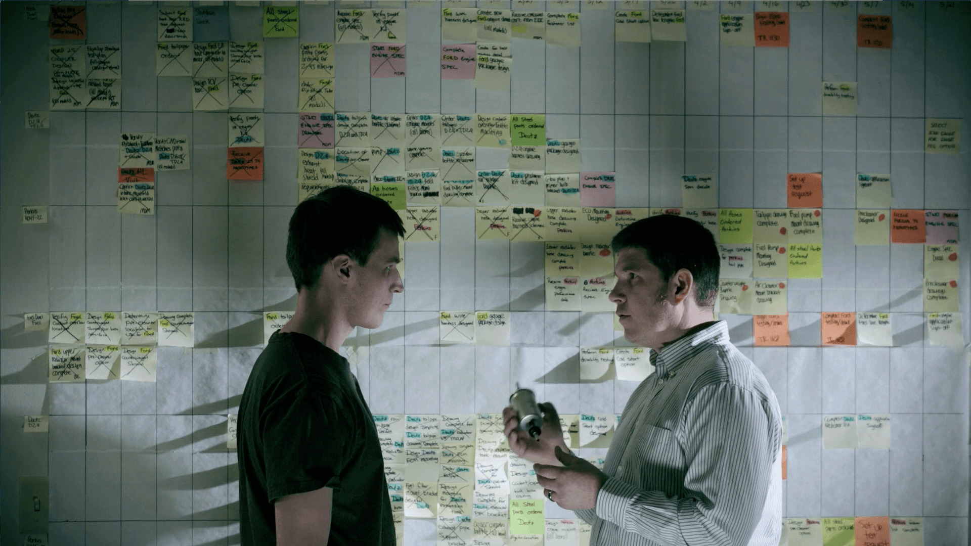 Genie Brand Film Engineers in Front of Post It Notes Two men are standing in front of a wall with sticky notes on it.