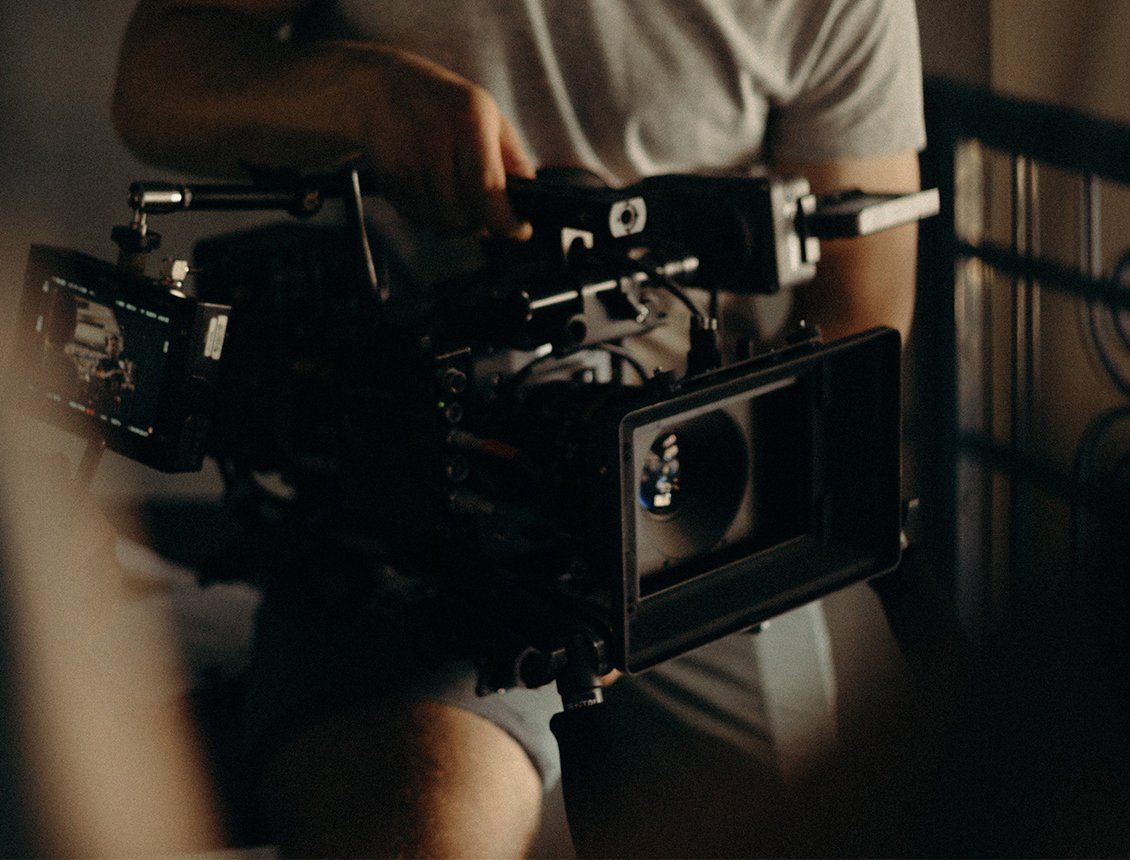 Image of a cameraman hand holding a cine style video production camera with matte box A man is holding a video camera in a dark room.