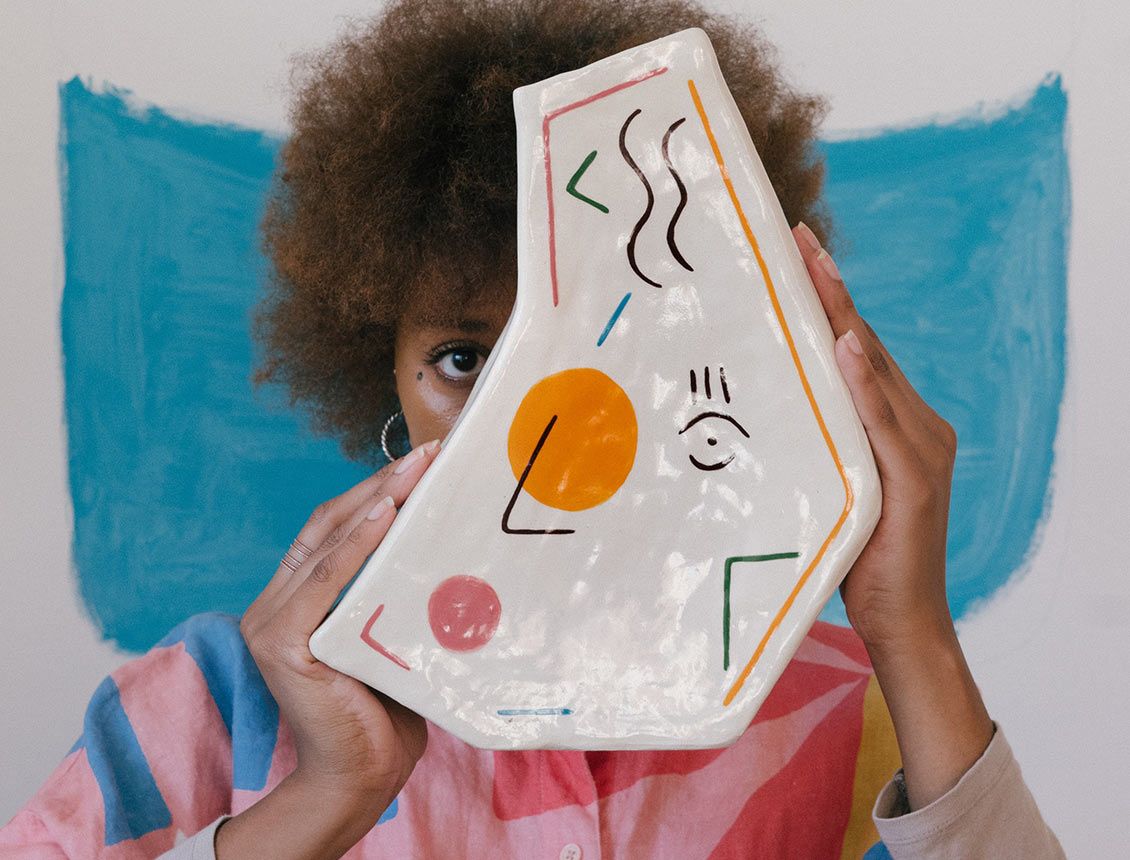 Photo of woman holding abstract art staring at camera A woman is holding a piece of art in front of her face.