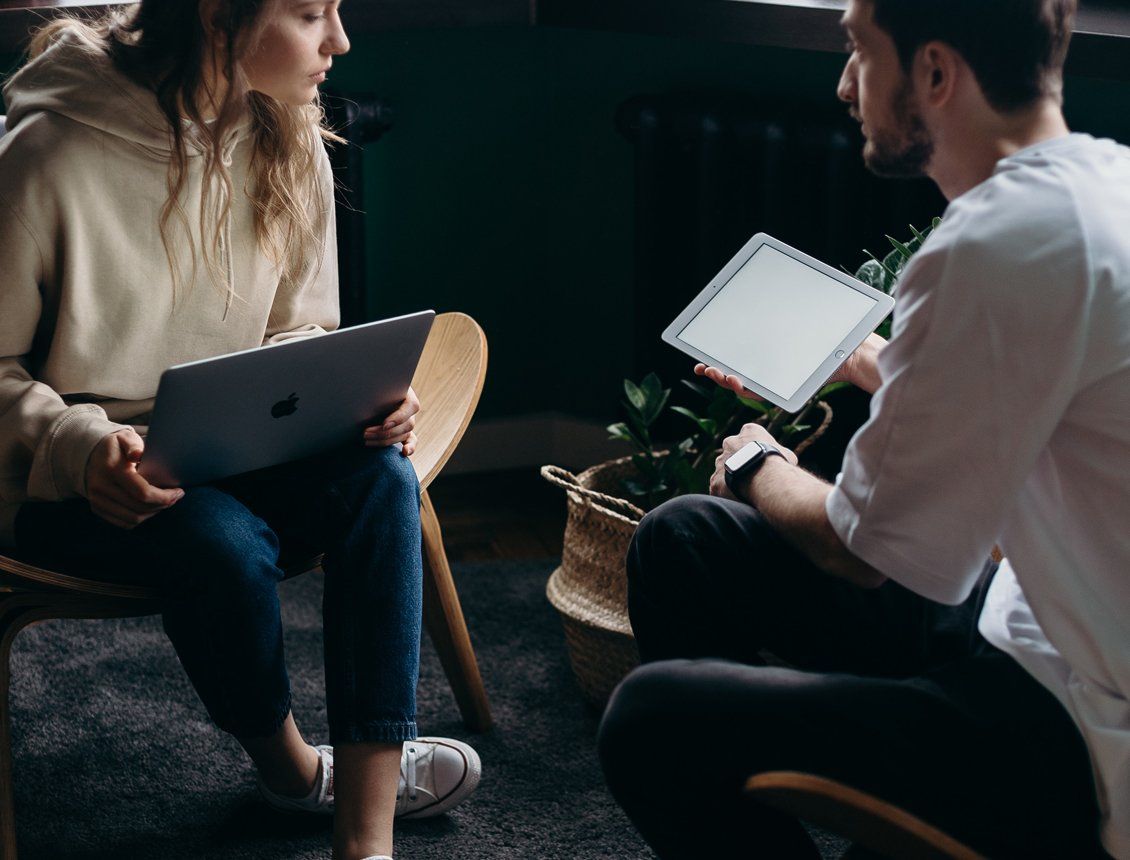 Image of man and woman in office discussing with laptop and tablet A man and a woman are sitting on the floor looking at a tablet.