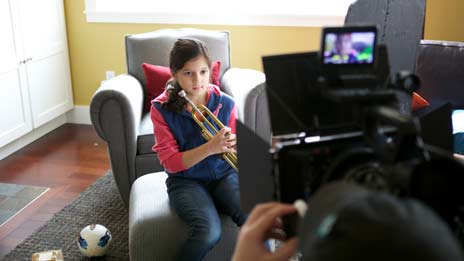 Spin Creative behind the scenes photo Treehouse brand video tv commercial shoot girl playing trumpet A young girl is sitting in a chair playing a trumpet.