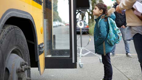 Spin Creative behind the scenes photo Treehouse brand video tv commercial shoot school bus girl waiting A little girl with a backpack is standing in front of a school bus.