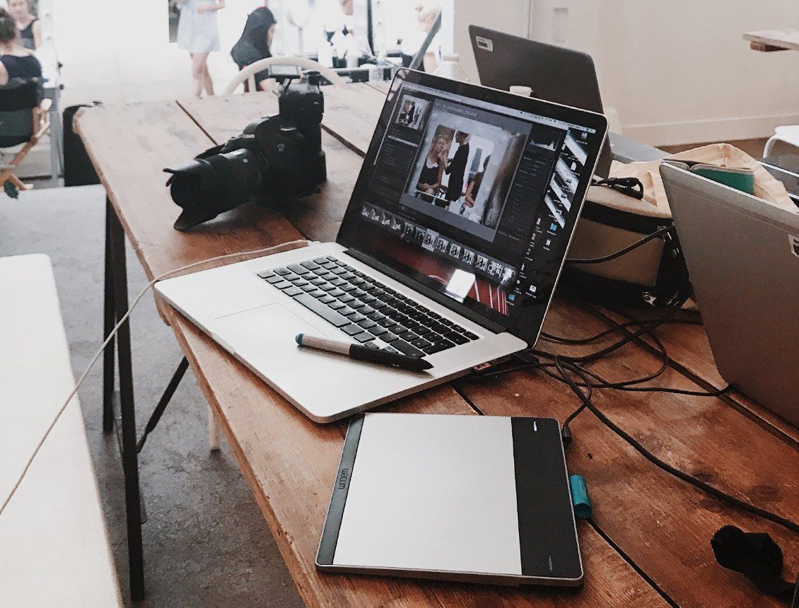 Image of a laptop, camera and tablet sitting on table in a creative agency A laptop computer is open on a wooden table