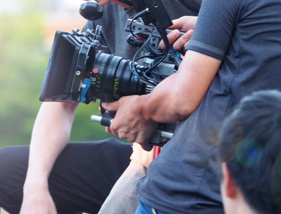 A person holding and operating a professional film camera, filming outdoors.