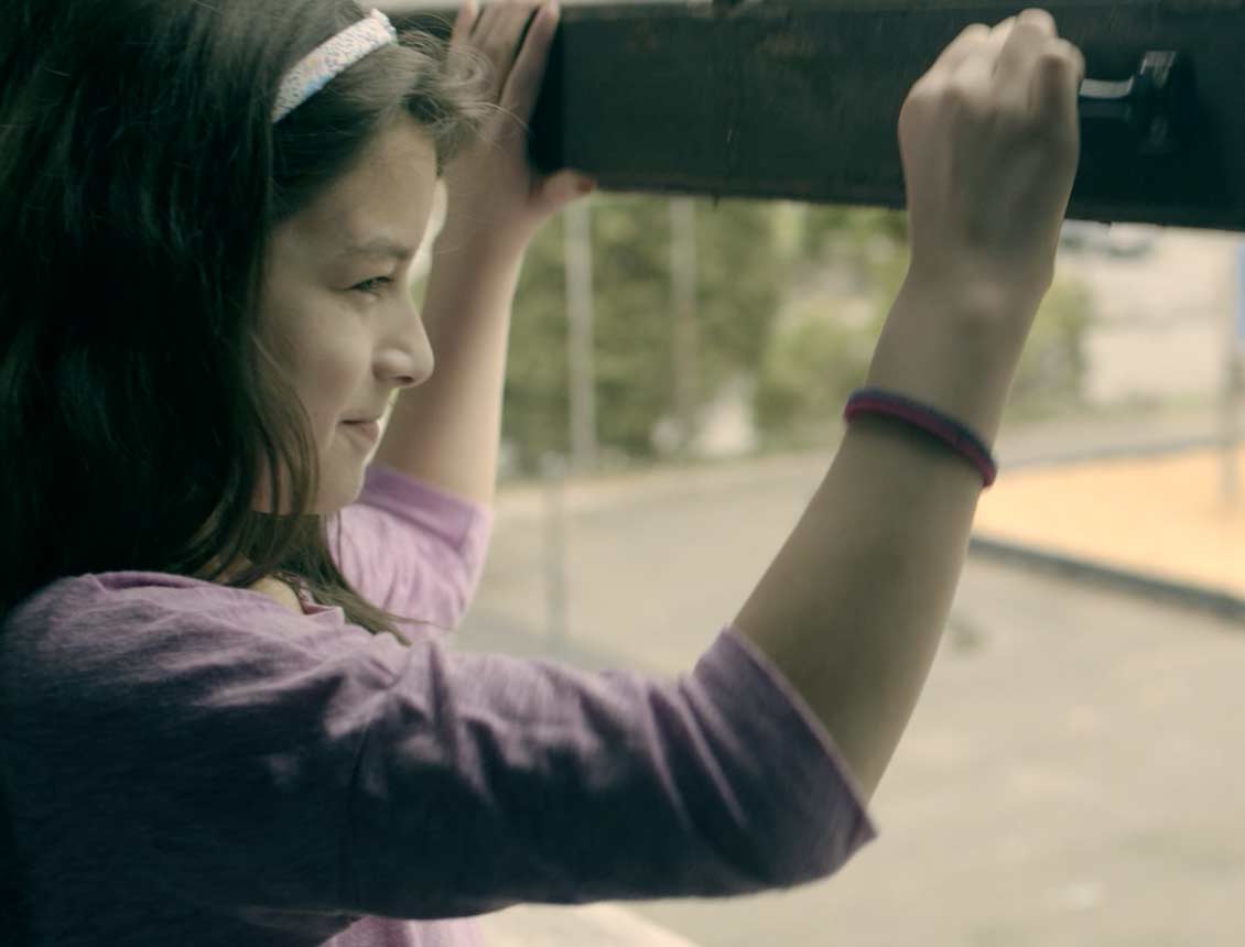 Woman opening a window, looking out with a smile. She's wearing a pink shirt and white headband.