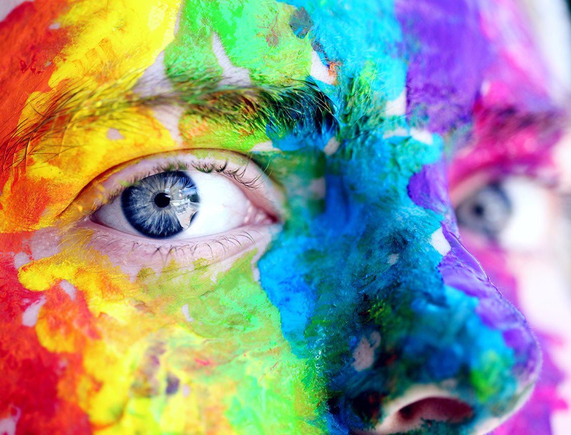 Close-up of a face covered in bright rainbow-colored paint; blue eyes.
