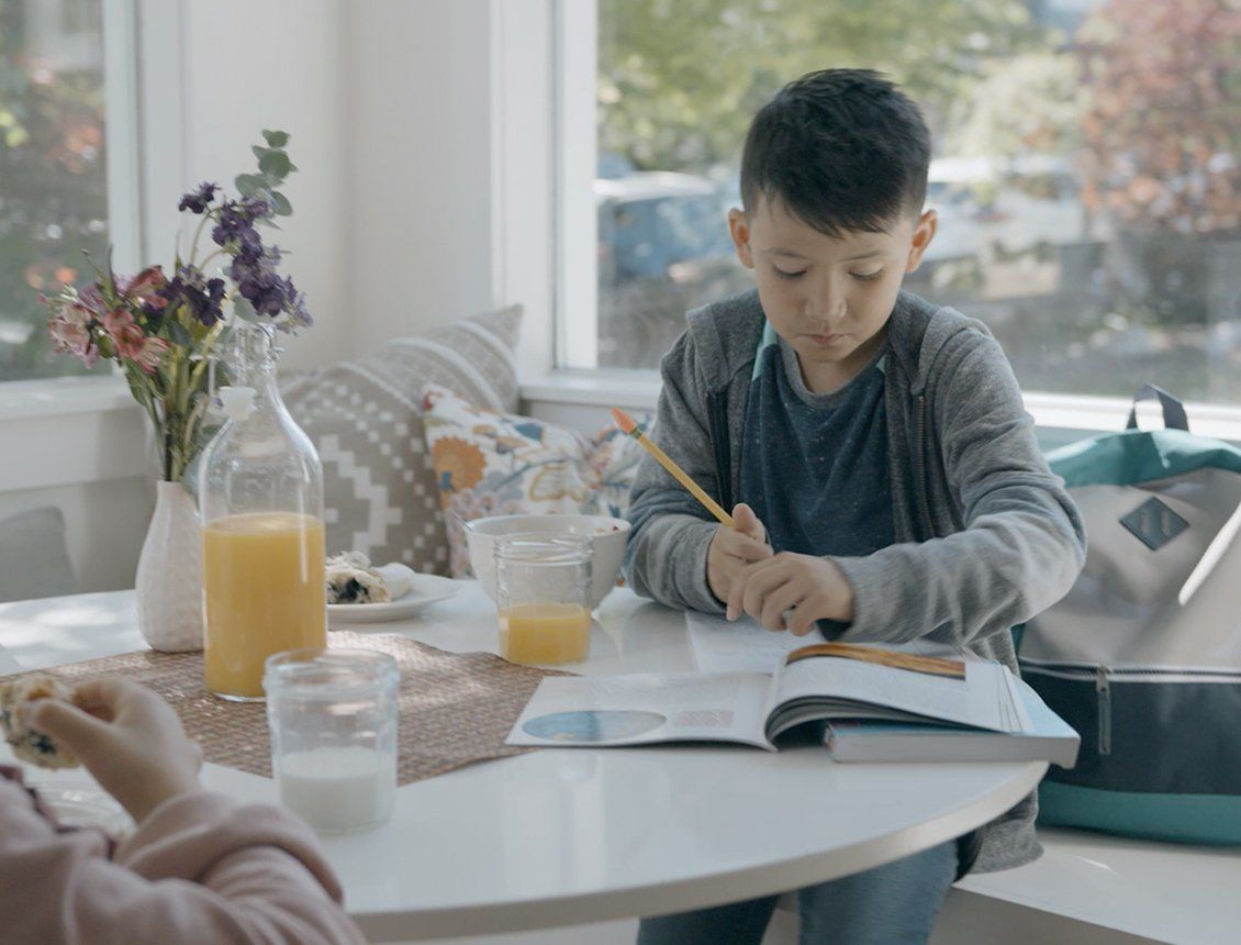 A young boy is sitting at a table with a book and a pencil.