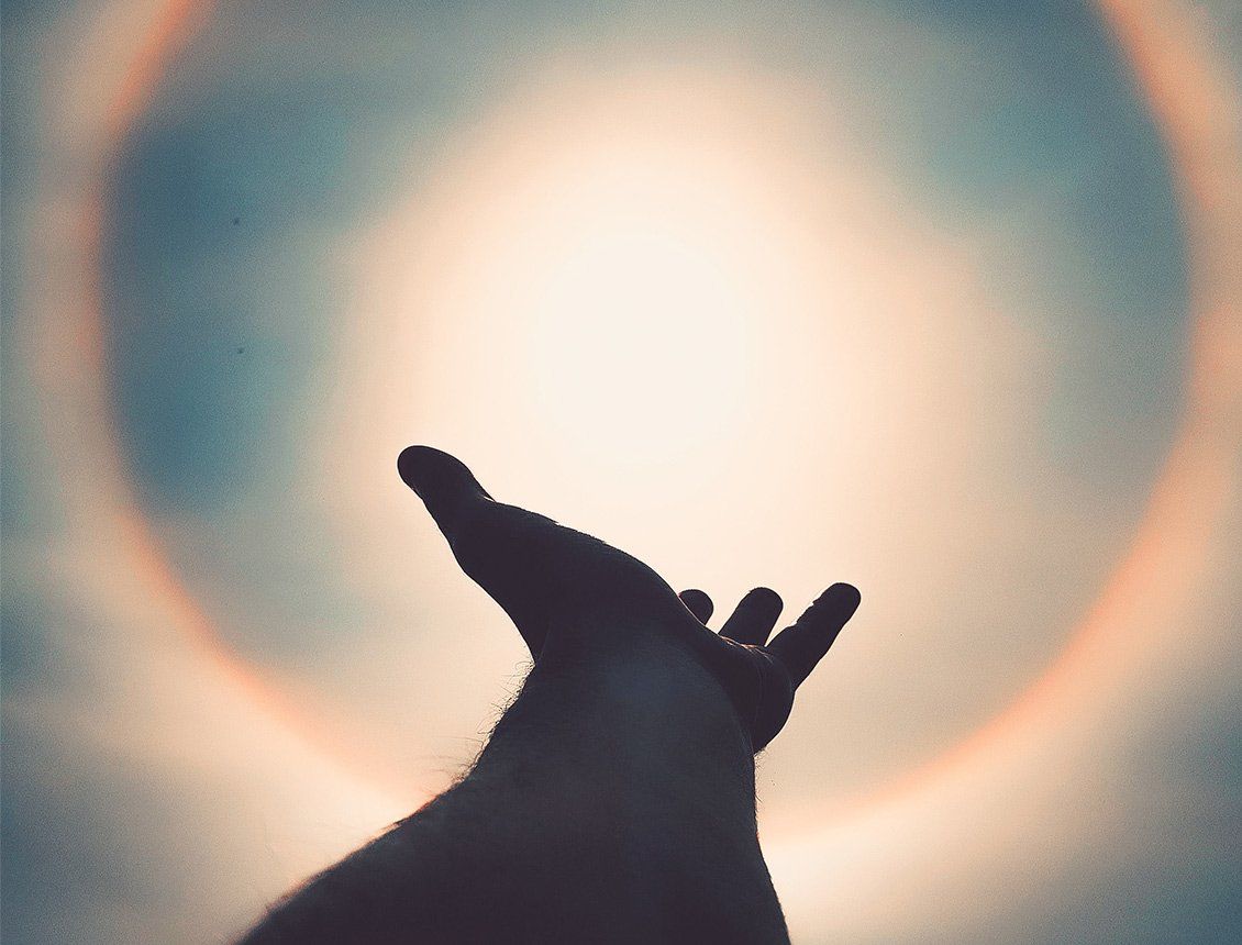 A hand is reaching out towards the sun with a rainbow in the background