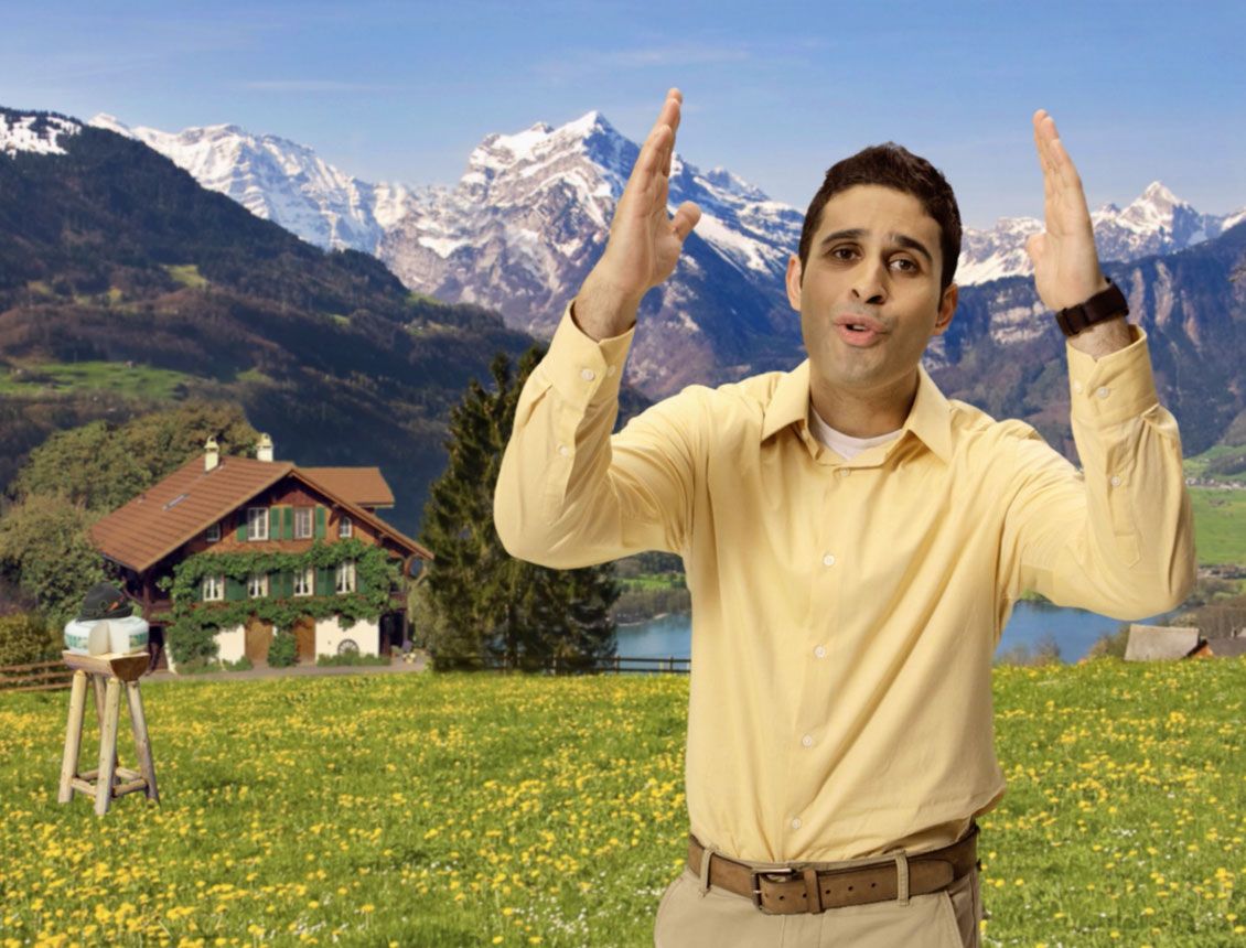 A man in a yellow shirt is standing in a field with mountains in the background