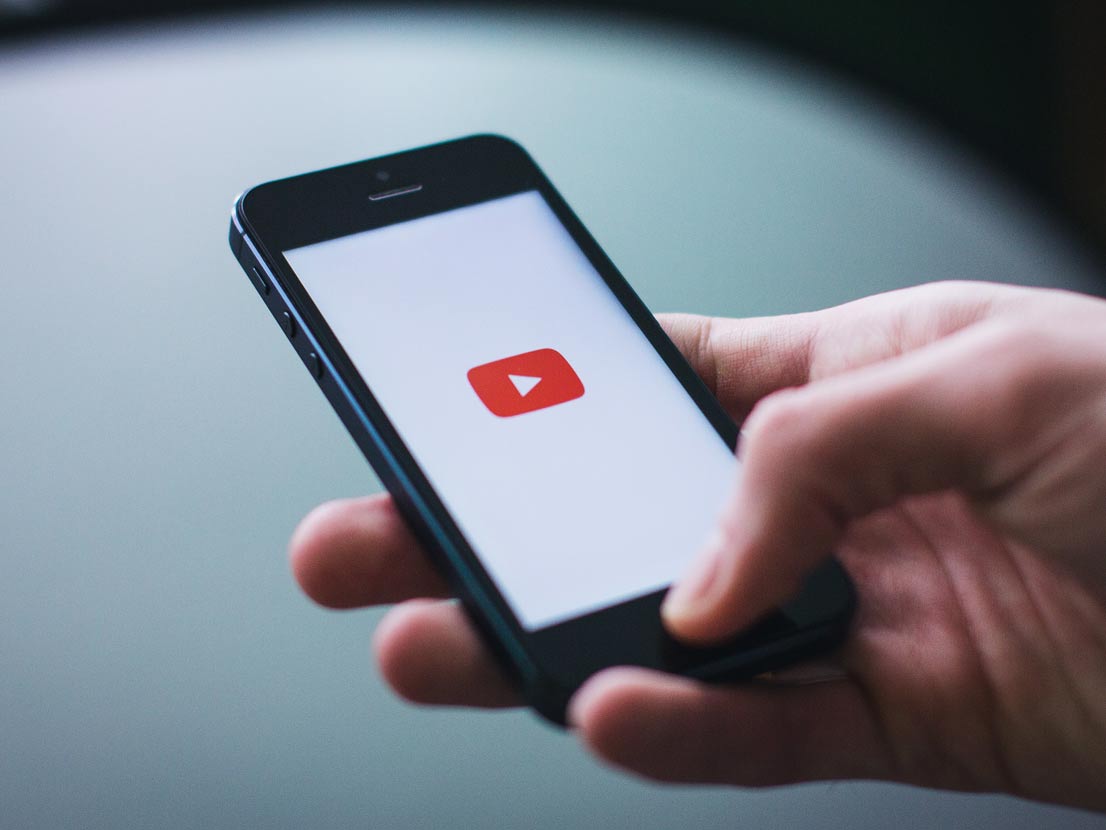 A person is holding a cell phone with a youtube logo on the screen.