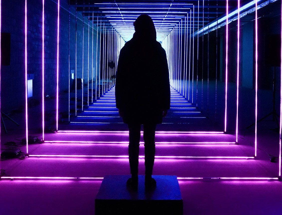 A silhouette of a person standing in a tunnel of neon lights.