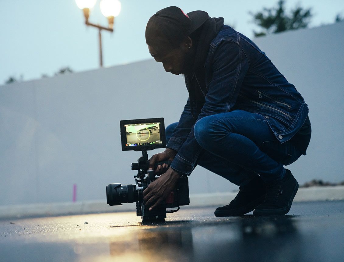 Image of man holding a cinema video camera with monitor on ground A man is kneeling down in front of a camera.