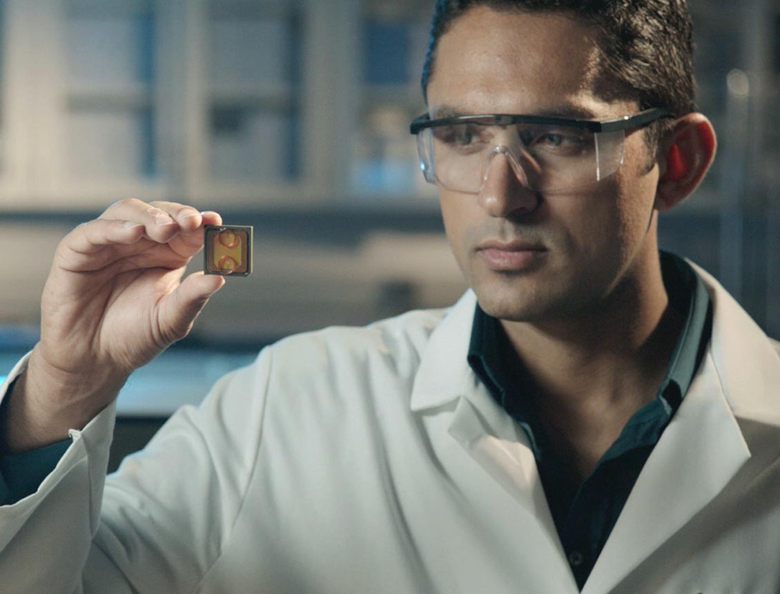 A man in a lab coat is holding a small piece of metal in his hand.