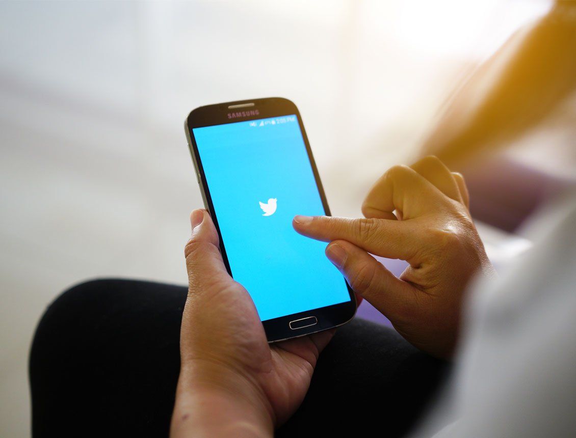 A person is holding a cell phone with a twitter logo on the screen.