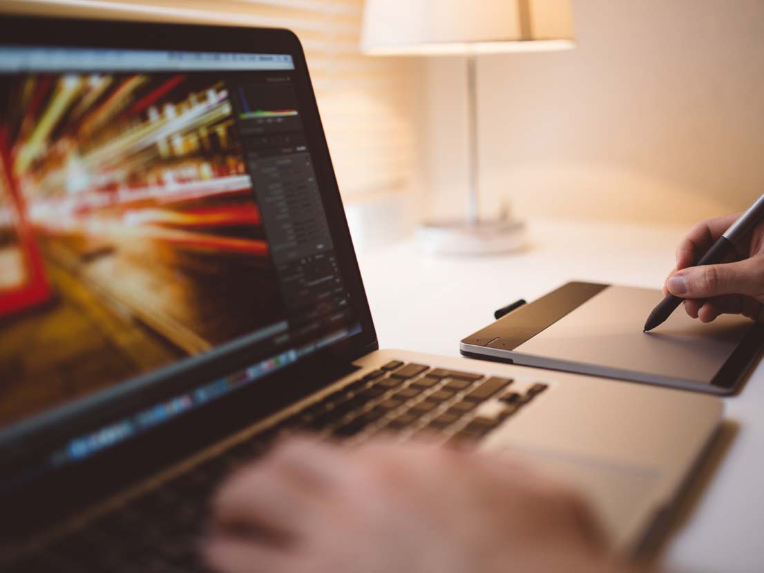 A person is using a laptop with a pen on a graphic tablet