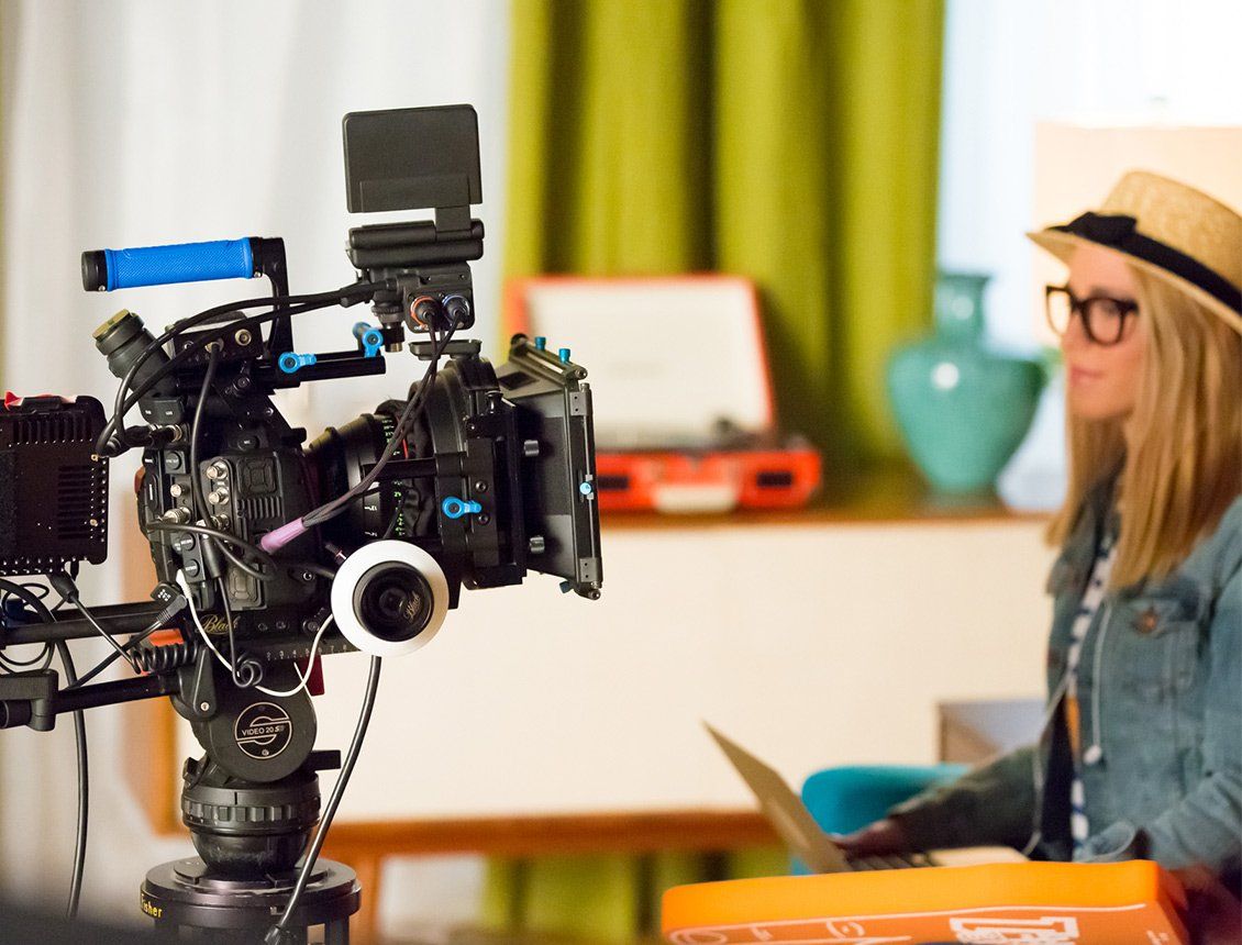 A woman is sitting in front of a camera while using a laptop.