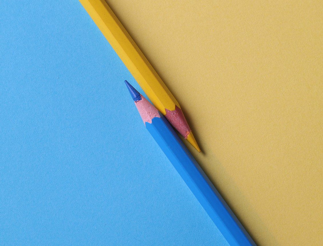 A yellow pencil and a blue pencil are sitting next to each other on a blue and yellow background.