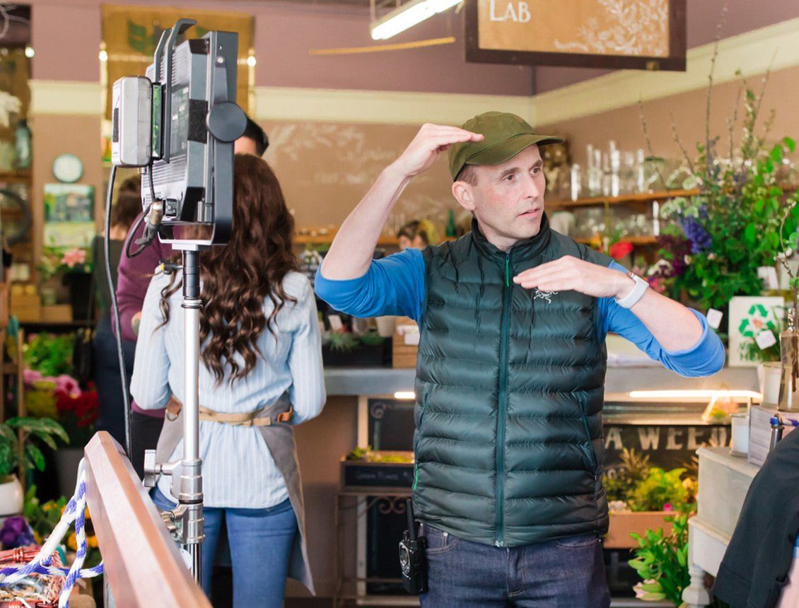 A man in a green vest is standing in front of a camera in a store.