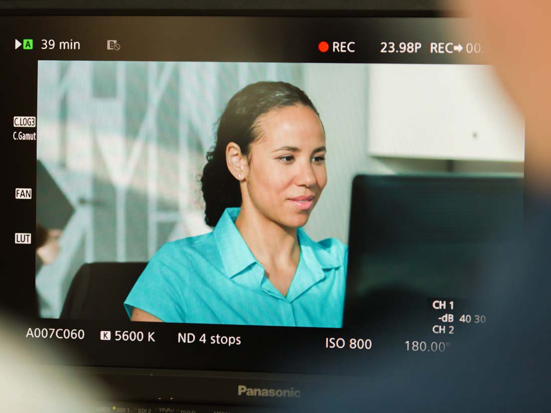 A woman in a blue shirt is sitting in front of a computer screen.