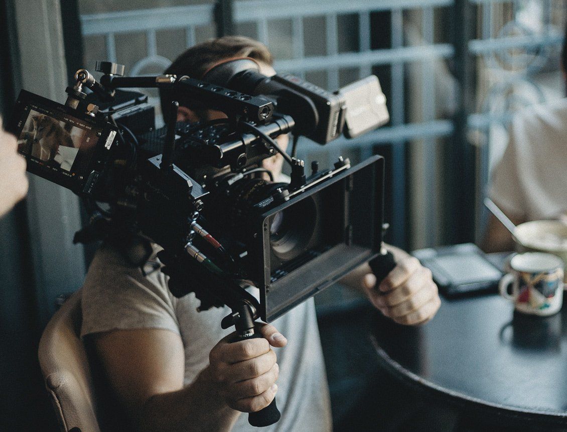 Person holding and operating a professional video camera, filming a scene at a table.