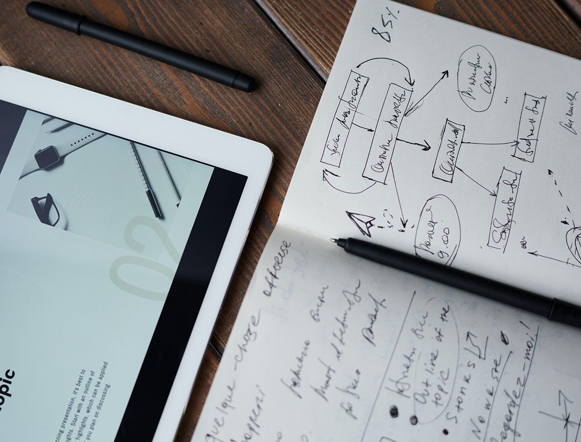 A tablet and a notebook are on a wooden table